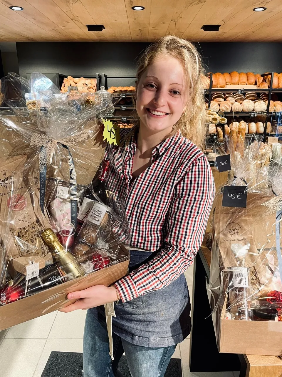 Jade, souriante, avec un panier cadeau dans sa boulangerie L’Héritage